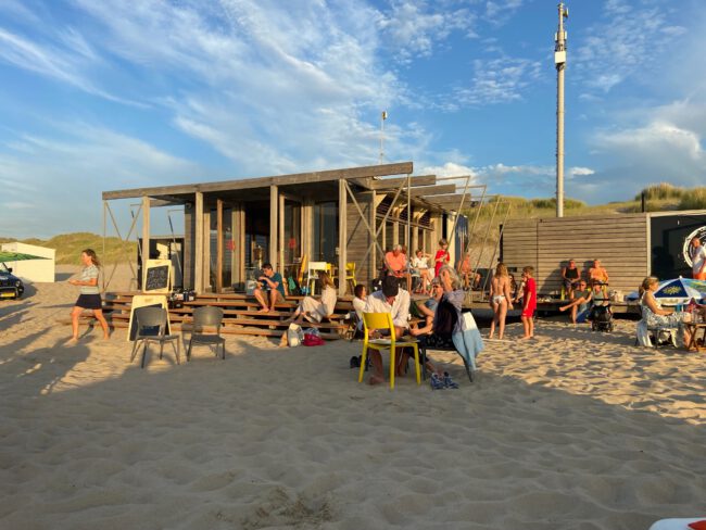 Gezellige sfeer bij het Zeecafé, waar bezoekers genieten van de zon op het strand met een drankje en goed gezelschap.