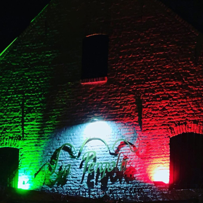 Buitenkant van La Pergola 's nachts verlicht met levendige groene en rode lichten.