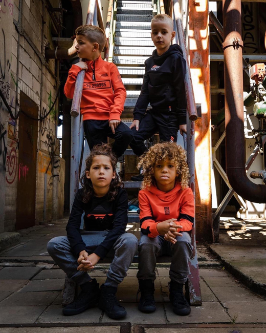 Kinderen in trendy kleding poseren in een stedelijk steegje met graffiti