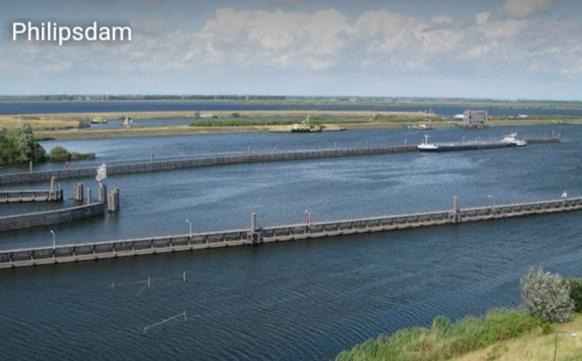 Uitzicht op de Philipsdam met passerende boten en uitgestrekte wateren onder een bewolkte hemel in Zeeland.