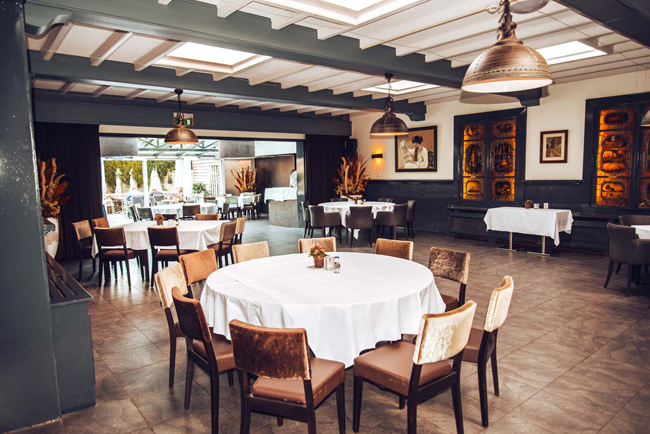 Eetzaal met wit gedekte tafels en bruine stoelen in Hotel Den Engel in Baarle Nassau