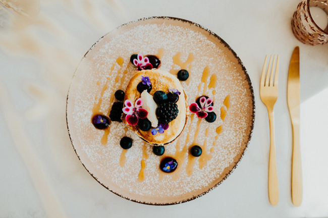 Pannenkoek versierd met verse bessen en eetbare bloemen, gepresenteerd op een keramisch bord, naast goudkleurig bestek bij Liefs Lies in Breskens