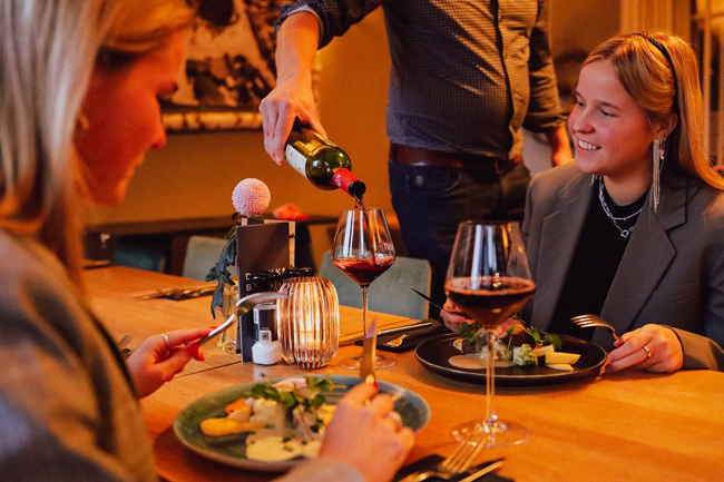 Serveerster schenkt wijn voor een gast aan een tafel met fijne gerechten bij Restaurant Bij Wout in Moergestel
