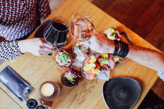Twee personen proosten met rode en rosé wijn boven een tafel met kleine gerechten bij Restaurant Bij Wout in Moergestel