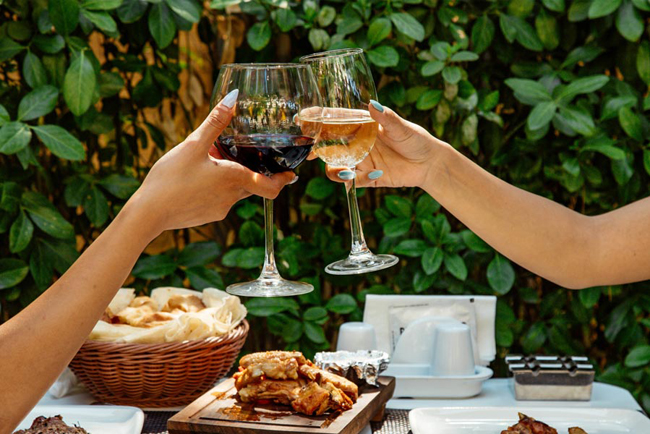 Twee personen proosten met rode en witte wijn bij een buitentafel met eten in Hotel Den Engel in Baarle Nassau