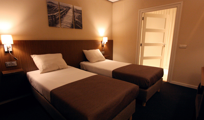 Tweepersoonskamer met bruine hoofdborden en wit beddengoed in Hotel De Bengel in Eersel