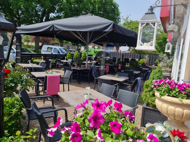 zonnig terras van pizzeria en grill la bella borger omgeven door bloeiende planten en comfortabele stoelen