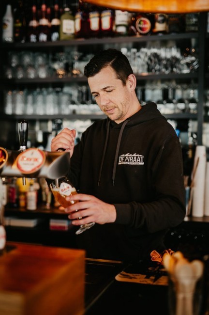 barman tapt biertje bij strandpaviljoen de piraat