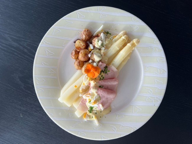 bord met witte asperges ham krieltjes en saus op donker tafelblad
