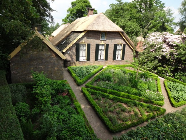 oude boerderij met rieten dak en klassieke moestuin vol bloeiende planten en struiken