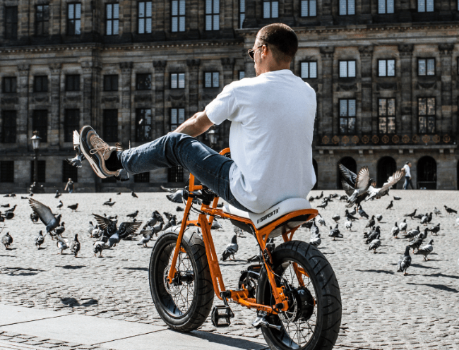 man rijdt relaxed op oranje lowrider tussen duiven op plein