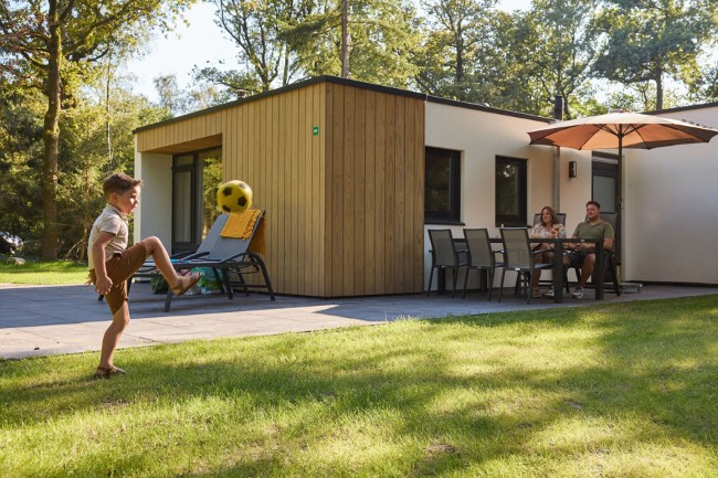 kind speelt voetbal terwijl ouders genieten bij de bungalow