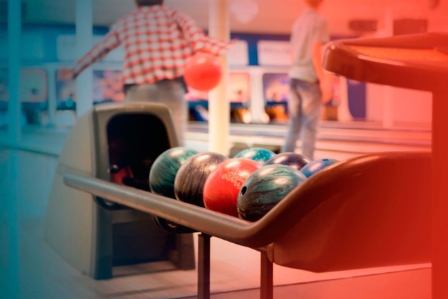 bowlingballen in rek met spelende mensen op de achtergrond