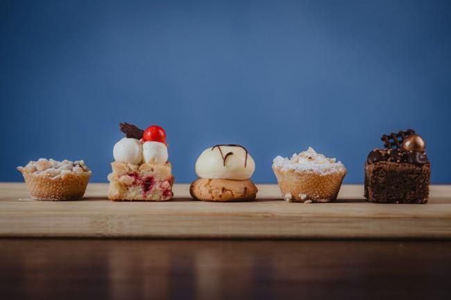 assortiment kleine gebakjes op houten plank met blauwe achtergrond