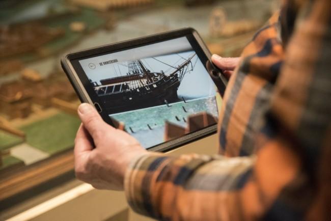 bezoeker gebruikt tablet om historisch schip in museum interactief te bekijken