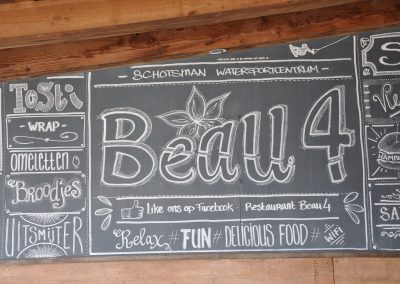 Groot krijtbord met handgeschreven Beau4, menu-teksten en krijttekeningen onder houten balken bij Restaurant & Terras Beau4