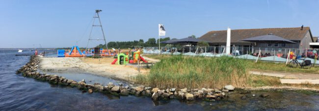 Kust met klein zandstrand en rotsen, speeltoestellen en opblaasbaar waterpark, terras met parasols bij Beau4