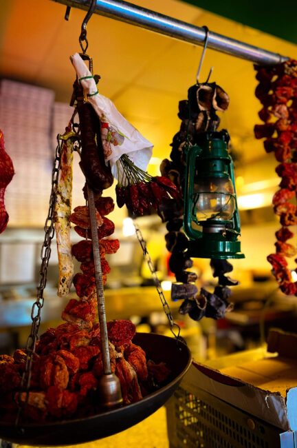 Gedroogde pepers, een gedroogde worst en een groene olielamp hangend boven een weegschaal, bij Pizzeria Napoli