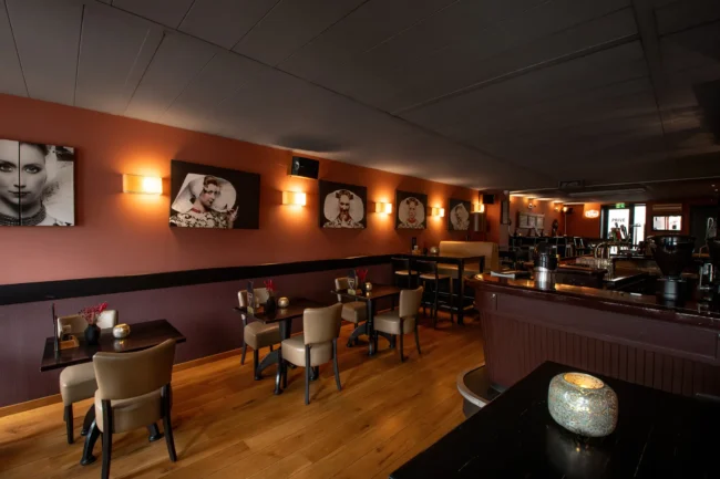 Interieur van verlicht eetcafé met houten vloer, tafels, stoelen, bar en wandkunst bij Eetcafé Hart van Tholen