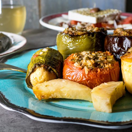 Turkoois bord met gevulde tomaat, gevulde groene paprika, gevulde courgette, stuk aubergine en gebakken aardappelparten bij K