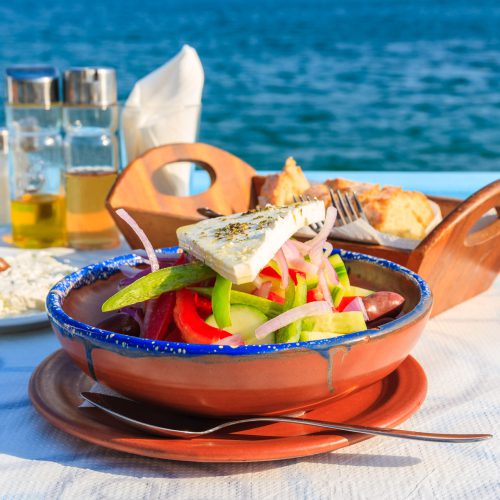 Griekse salade met feta, olijven, paprika en ui in terracotta kom op tafel aan zee, bij Kreta Steenbergen