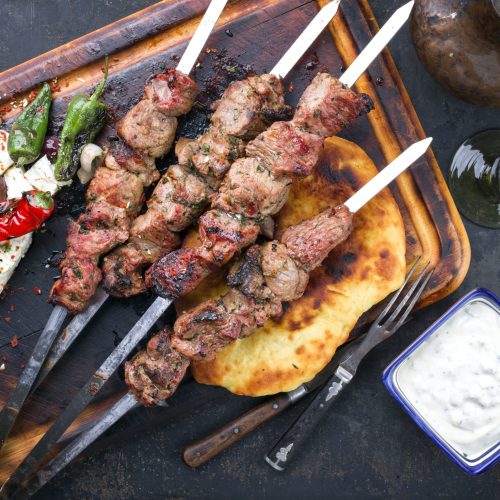Vier gegrilde vleesspiesjes op metalen prikkers met platbrood, gegrilde pepers, feta en witte dip bij Kreta Steenbergen